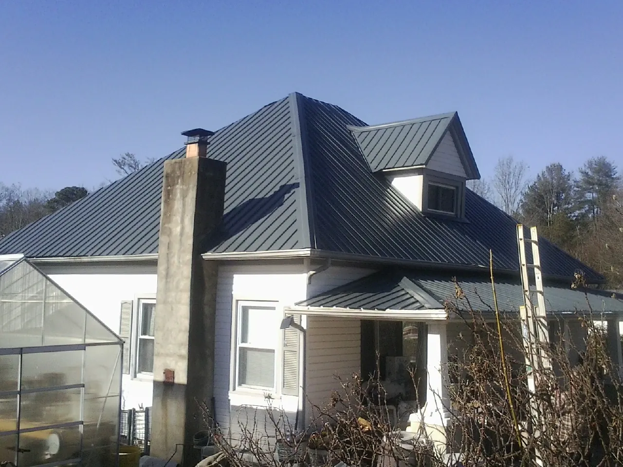 Dark blue standing seam metal roof on a white farmhouse with dormer — Slate & Tile Roof Repair by Roofing Brothers in Hellertown