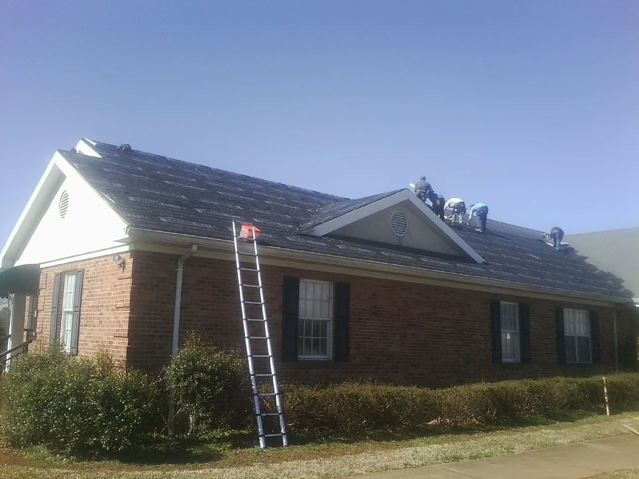 Crew tearing shingles off a brick ranch roof with a ladder set — Emergency Roof Repair work by our crew in Hellertown