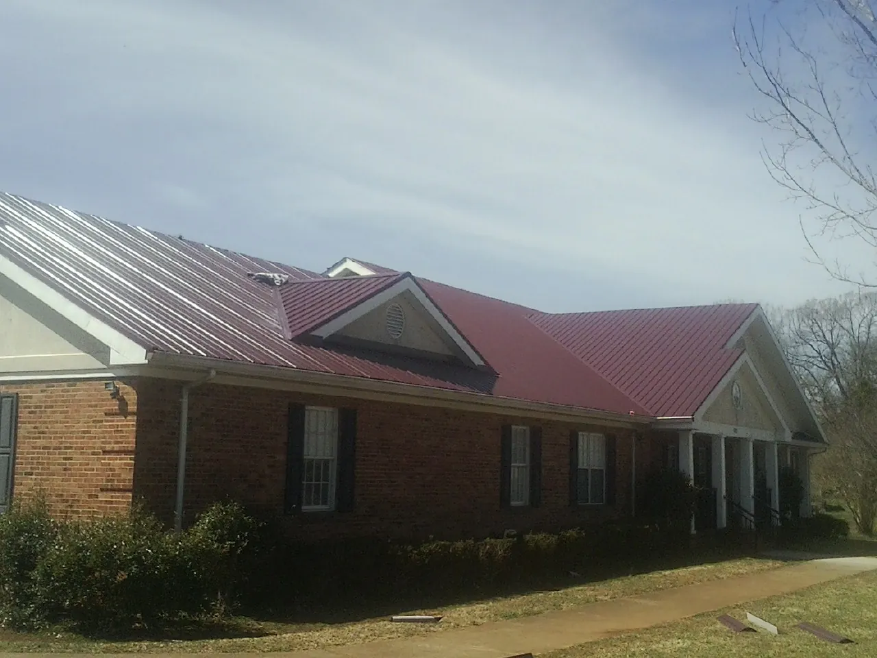 Red metal roof with gabled entries on a long brick building, from a Hail Damage Roof Repair job in Hellertown
