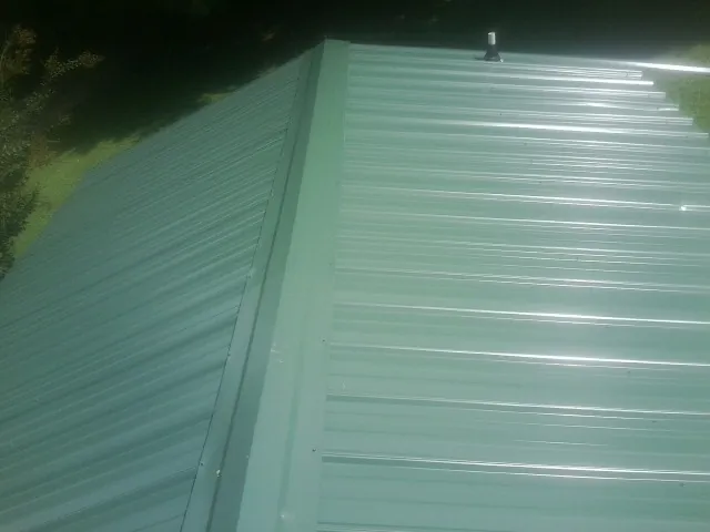New green metal panels meeting at the ridge of a roof — Flat Roof Repair work by our crew in Hellertown