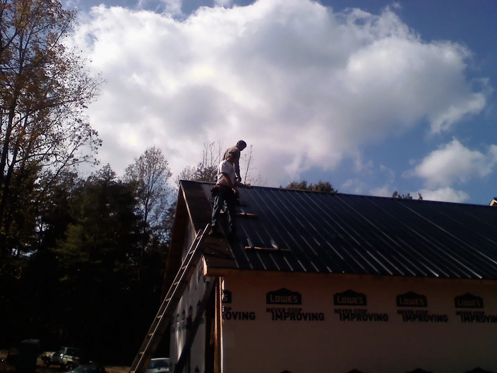 Roofer fastening dark metal panels high against a cloudy sky, from a Roof Inspection job in Hellertown