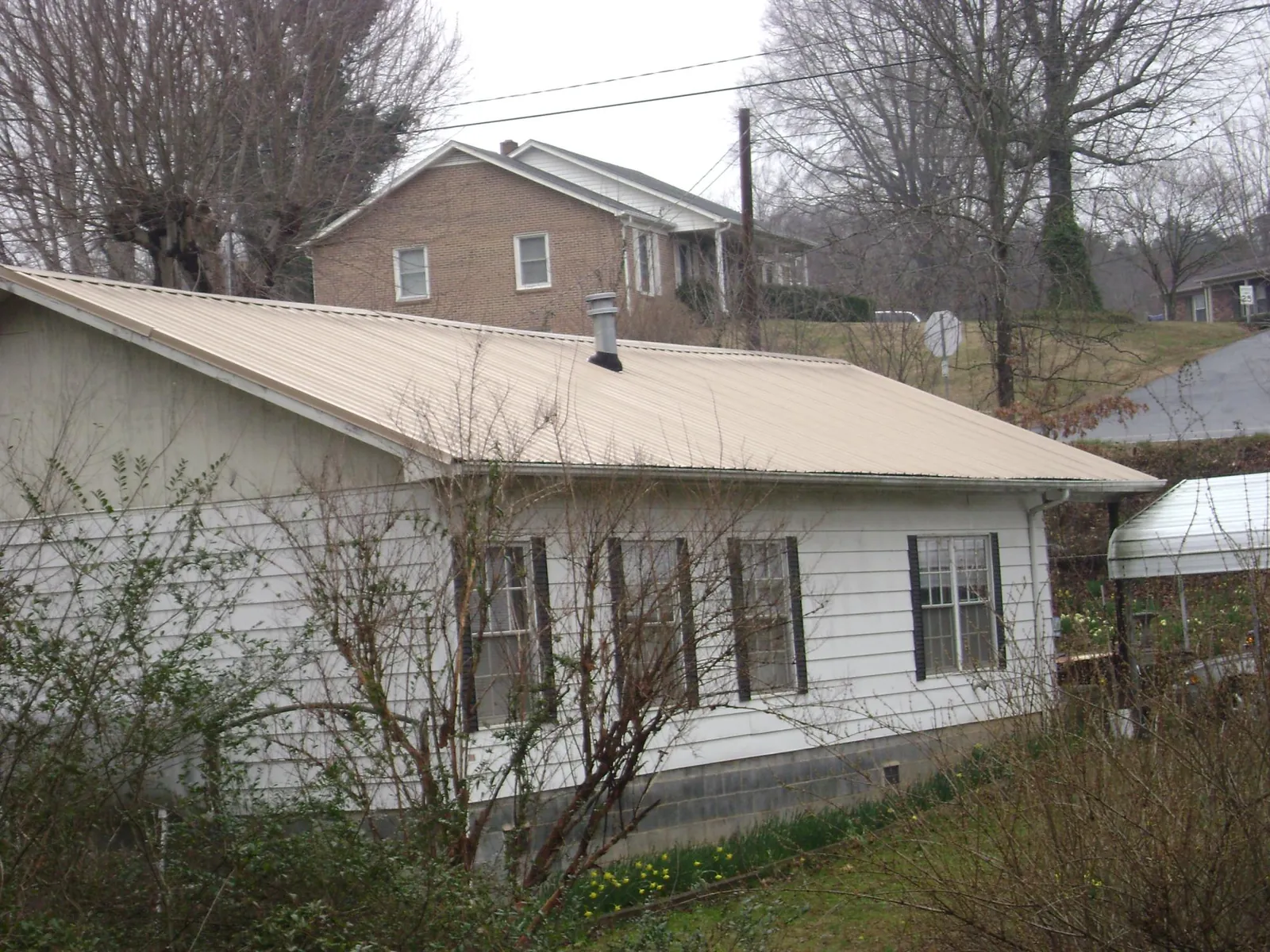 Tan metal roof on a white sided house set into a hillside — Commercial Roofing by Roofing Brothers in Hellertown